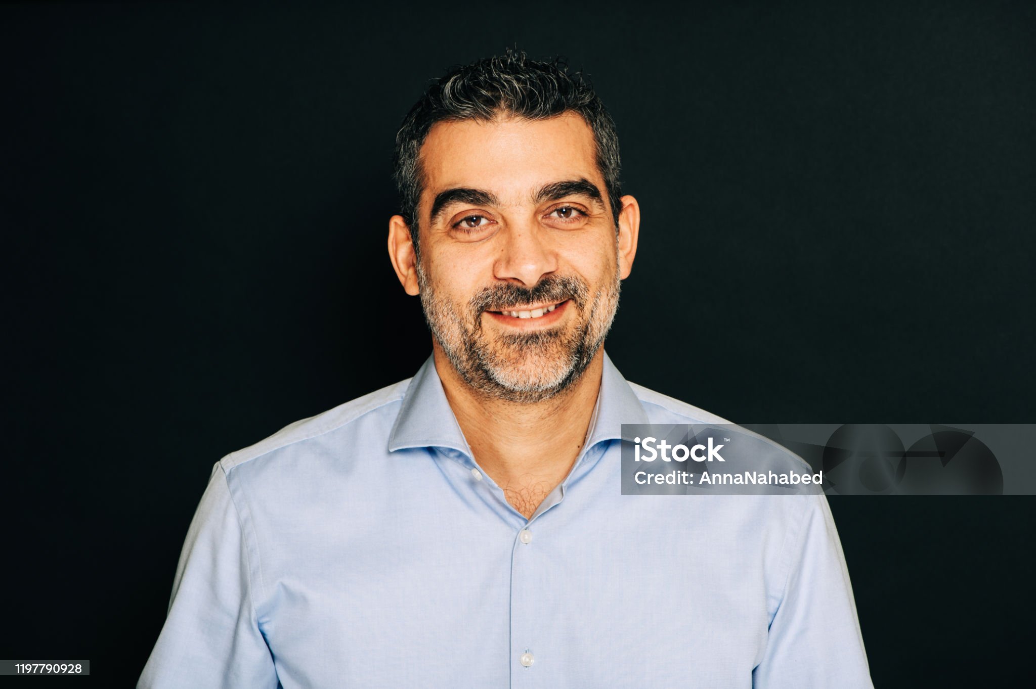 Studio portrait of handsome man wearing formal blue shirt, posing on black background